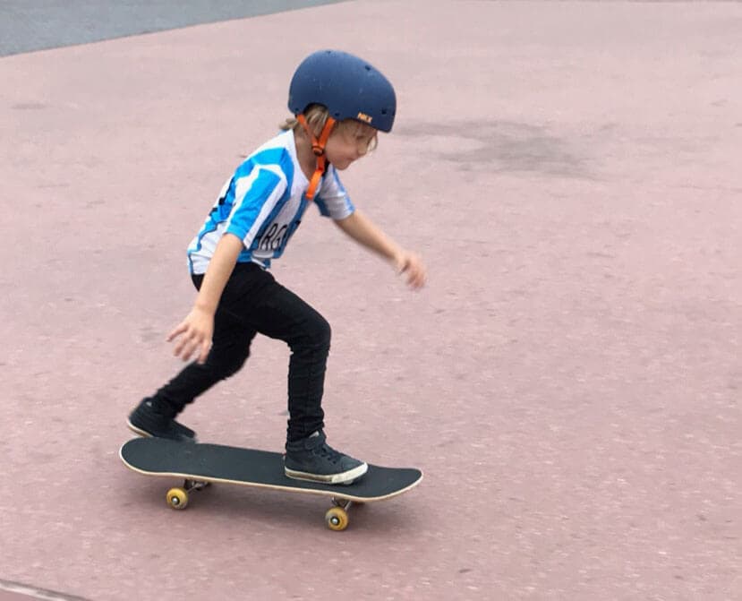 En lille dreng der står på skateboard.
